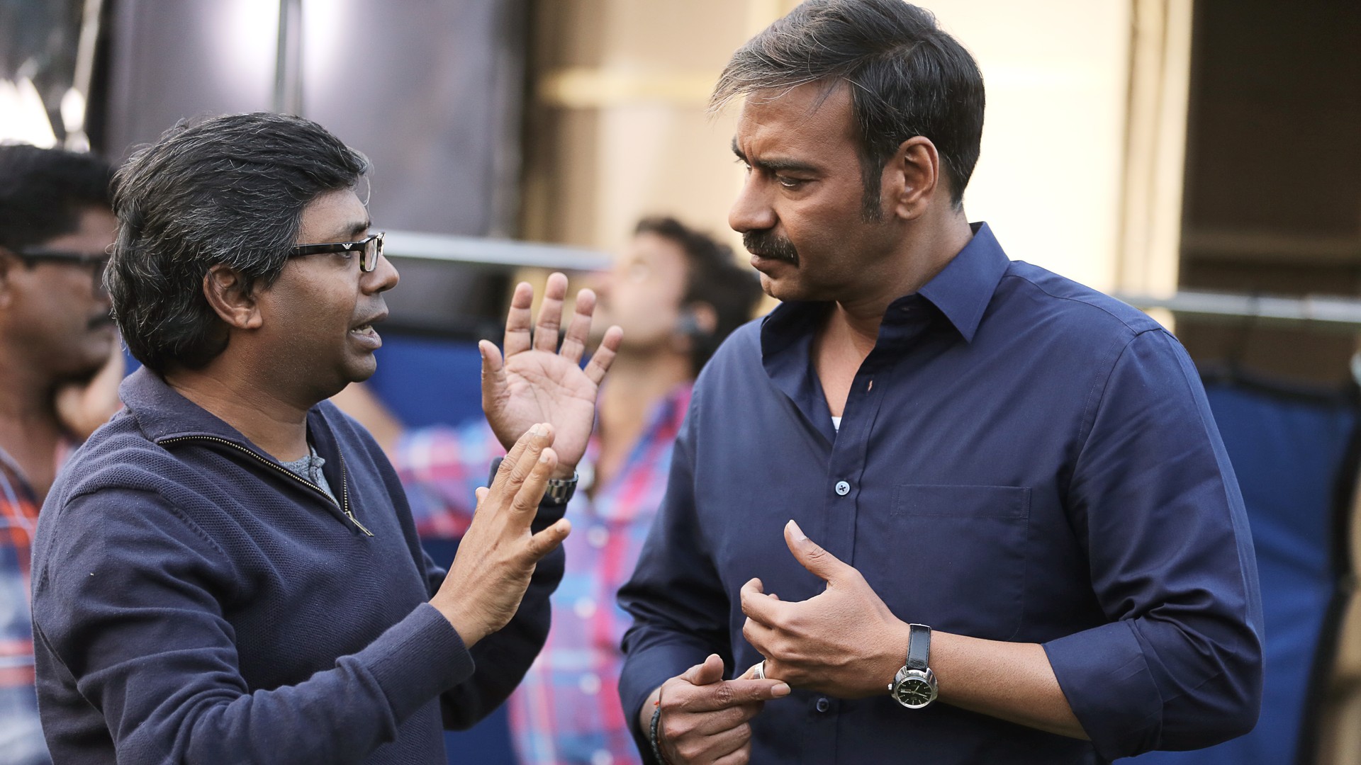 Ajay Devgn in a navy shirt listening to director Raj Kumar Gupta, who gestures as he talks, on the set of the film Raid in 2017