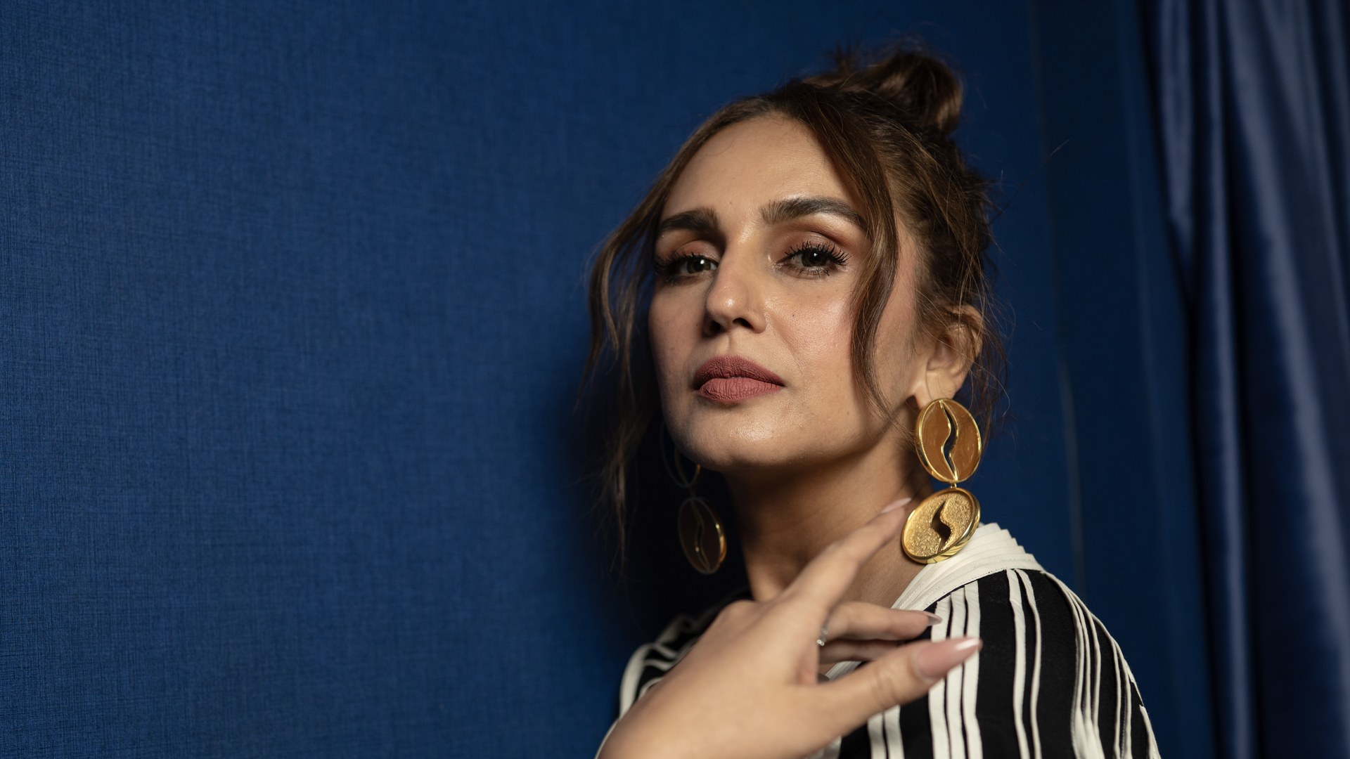 Huma Qureshi posing against a blue backdrop in a black and white striped outfit and large gold earrings at the 2025 Toronto International Film Festival