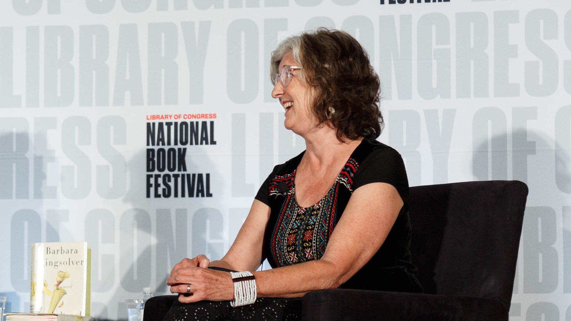 Barbara Kingsolver laughing while seated onstage in a black embroidered top at the Library of Congress National Book Festival in Washington, D.C., in 2019