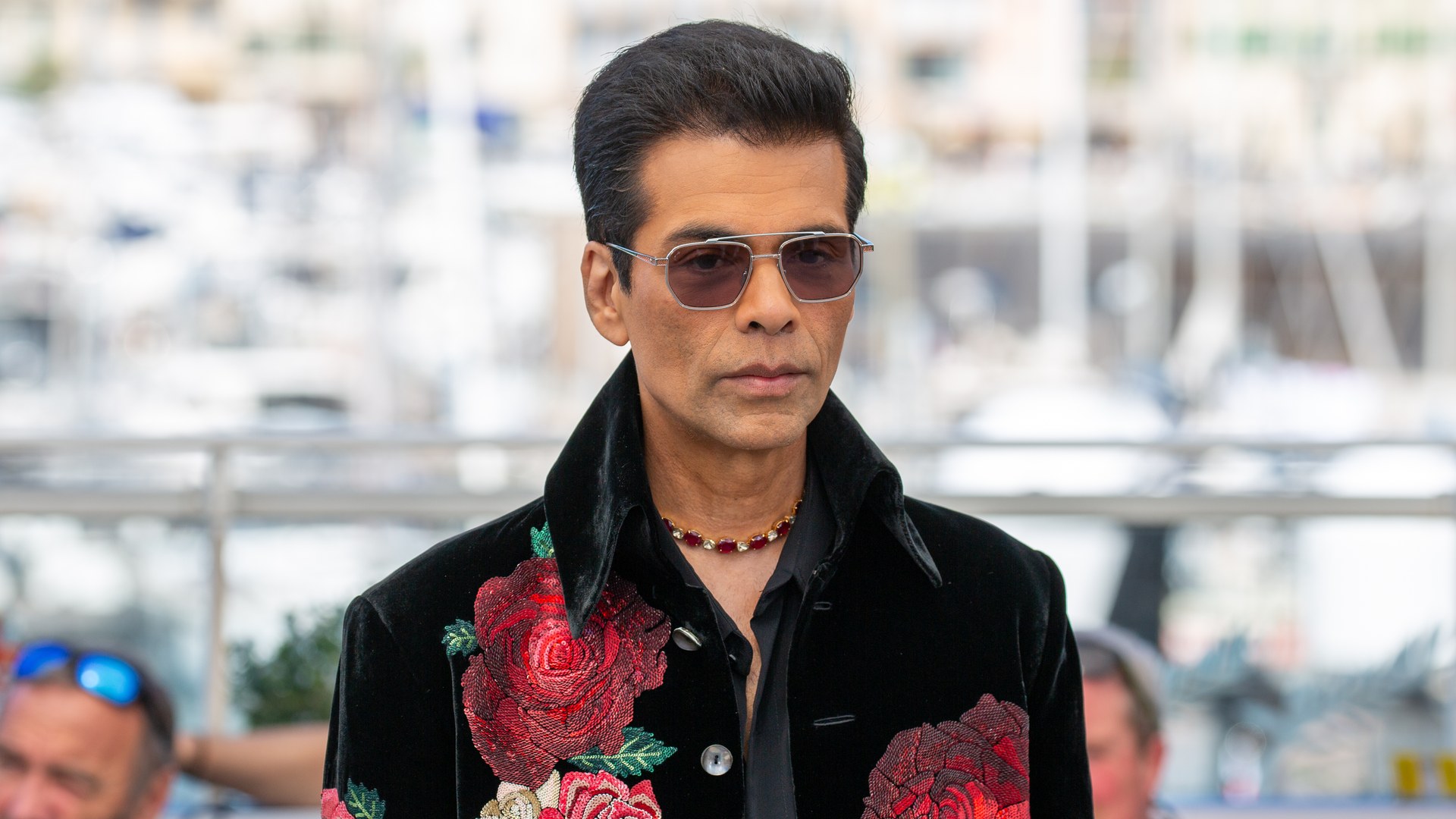 Karan Johar in tinted aviator sunglasses and a black velvet jacket embroidered with red roses at a photocall at the 2025 Cannes Film Festival