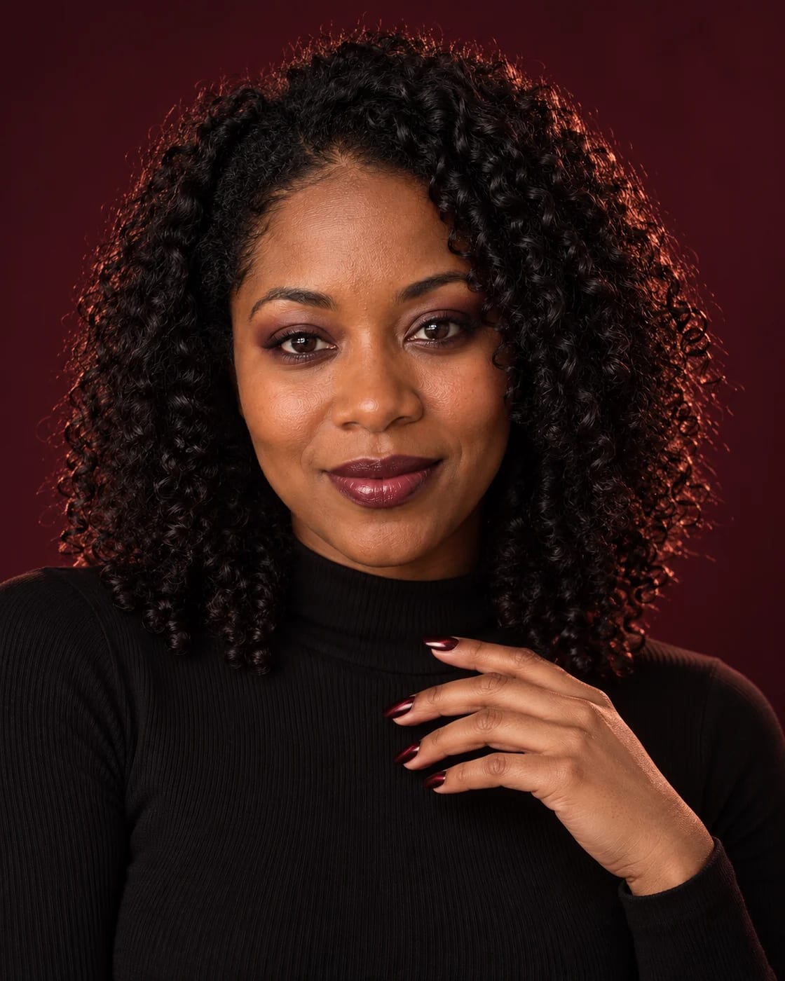 A fictional curly-haired woman with a deep berry lip and dark-red reflective manicure against a burgundy studio background.