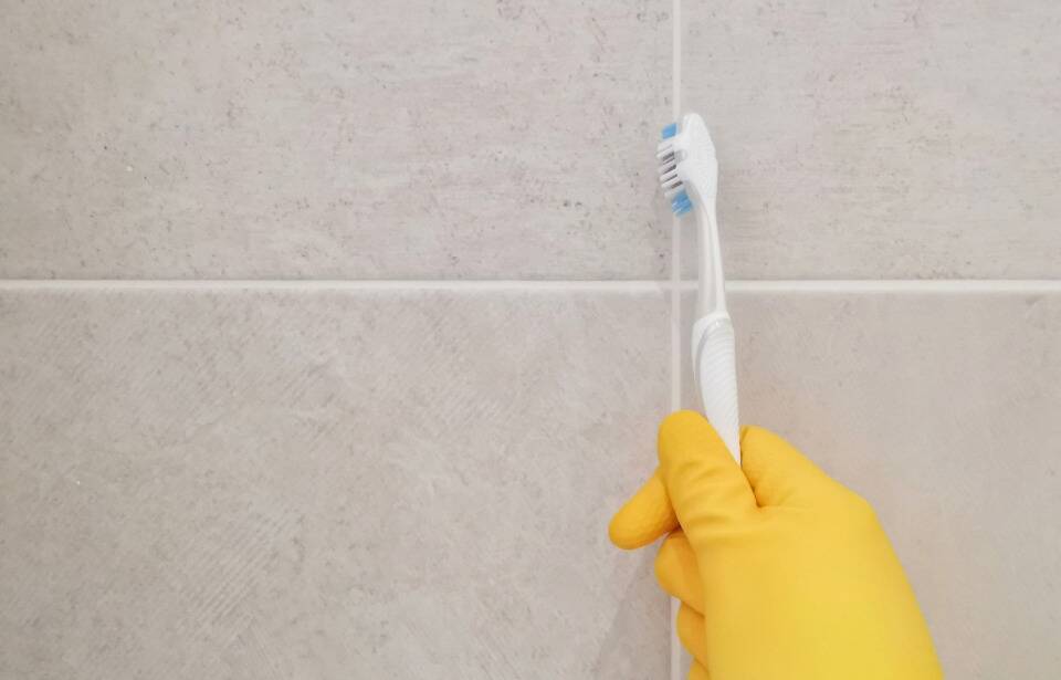 old toothbrush scrubbing tile grout
