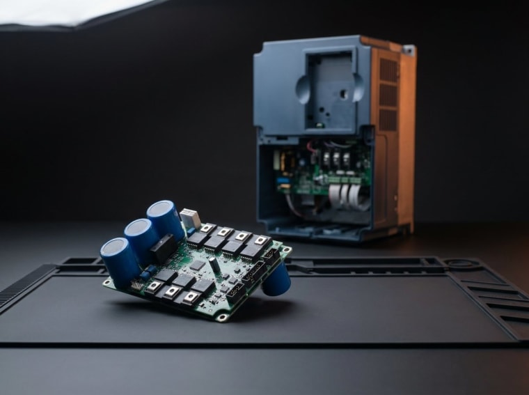 VFD invertor təmiri — arxada tezlik çeviricisi, önündə IGBT modulu və DC bus kondensatorları
