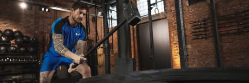 Mann in Sportkleidung schlägt mit Hammer auf Traktorreifen im Fitnessstudio