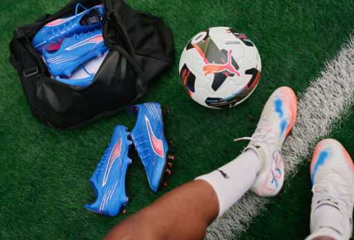 Drei Paar Puma Untamed Fussballschuhe und eine Fussballtasche auf dem Rasen.