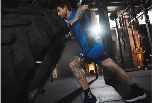 Person im Fitnessstudio schiebt großen Reifen, umgeben von Trainingsgeräten und dramatischer Beleuchtung.