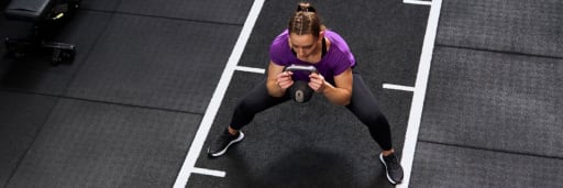 Person macht Kettlebell-Übung im Fitnessstudio auf schwarzer Matte mit weißer Markierung.