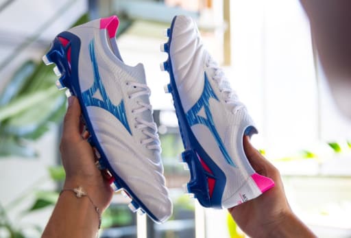 Ein Mann haelt ein Paar Mizuno Urban Electric Fussballschuhe in der Hand.