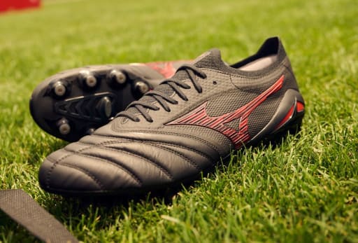 Ein schwarzer Mizuno Shadow Gem Fussballschuh mit roten Akzenten.