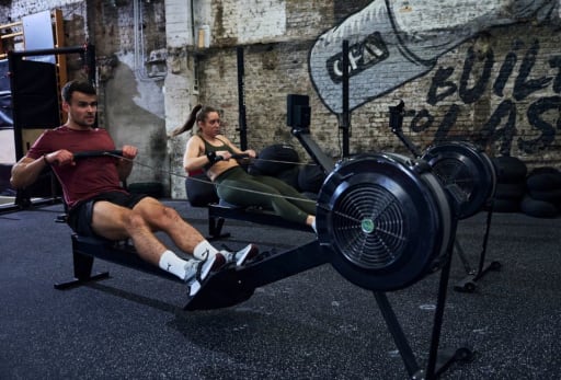 Eine Frau und ein Mann rudern im Firnessstudio.