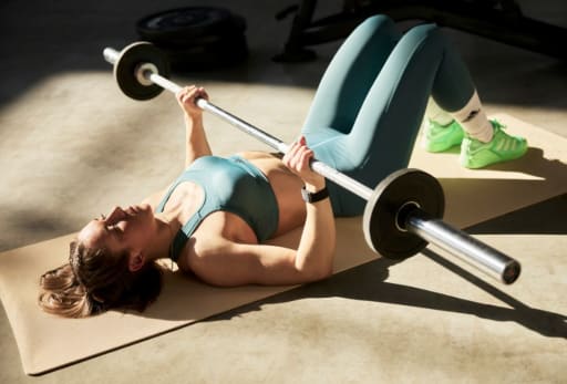 Person hebt Langhantel auf Trainingsmatte in Sportkleidung.