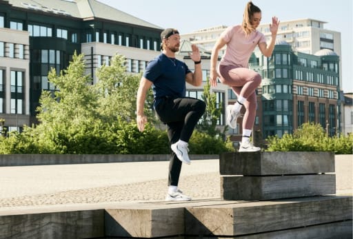 Outdoor-Workout mit zwei Personen auf Holzplattformen, moderne Kulisse im Hintergrund.