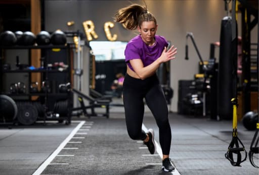 Person in Sportkleidung beim Sprinttraining in einem Fitnessstudio mit Geräten und ARC-Schriftzug im Hintergrund.