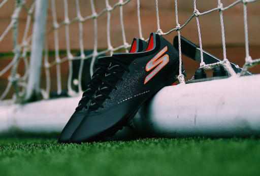 Ein Paar Skechers Obsidian Fussballschuhe lehnt an einem Fussballtor.