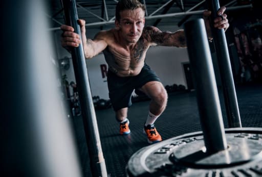 Mann schiebt Schlitten im Fitnessstudio.