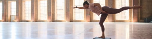 Person macht Yoga-Pose in hellem, geräumigem Raum mit hohen Fenstern und Backsteinwänden.