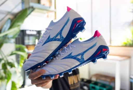 Ein Mann haelt ein Paar Mizuno Urban Electric Fussballschuhe in der Hand.