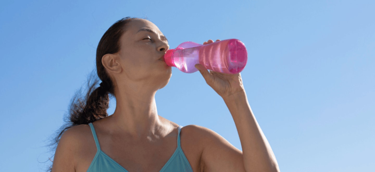 Kobieta stojąca na dworze pije wodę gasząc pragnienie