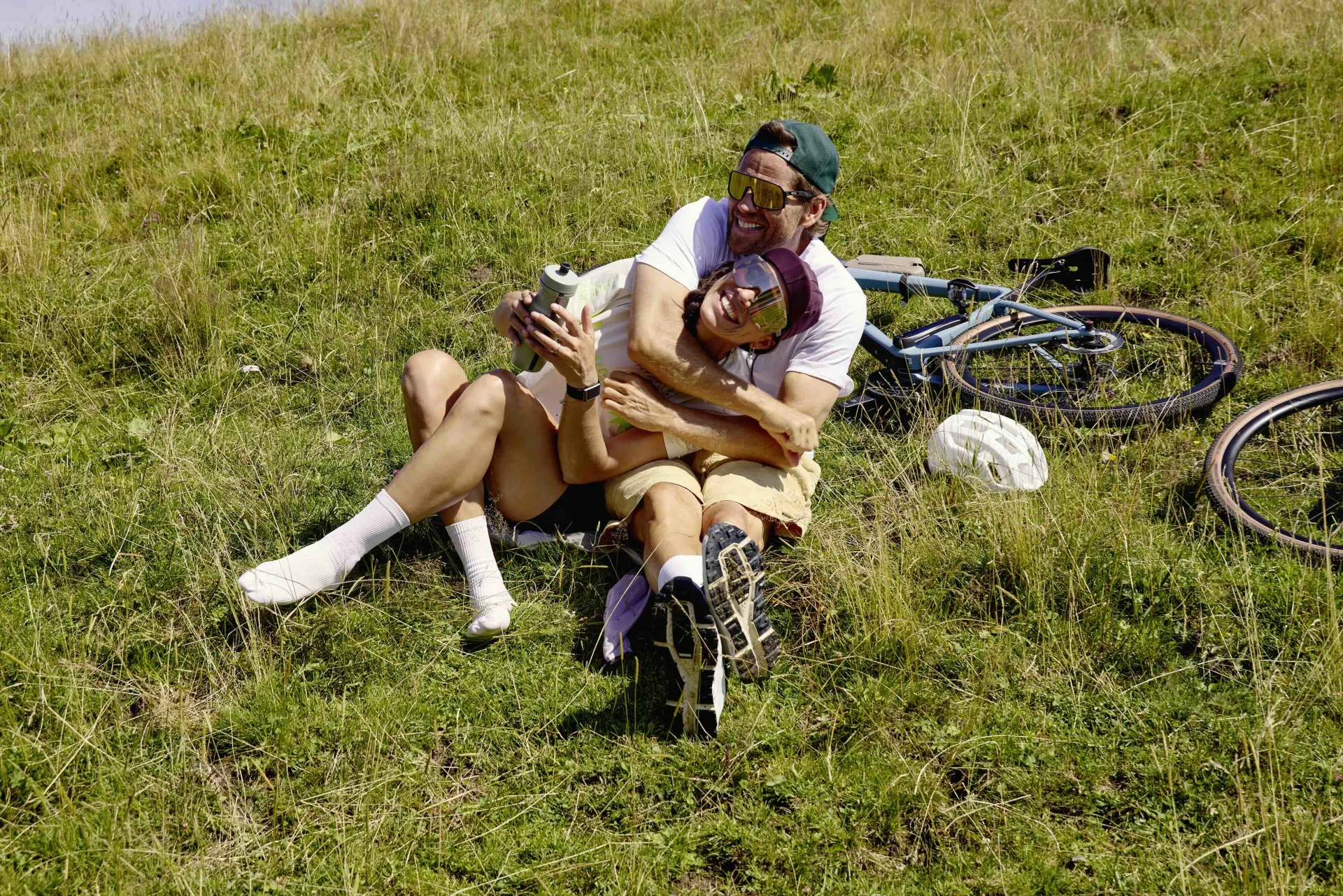 Eine Frau und ein Mann sitzen umschlungen im Gras. Dahinter liegt ein Gravelbike.