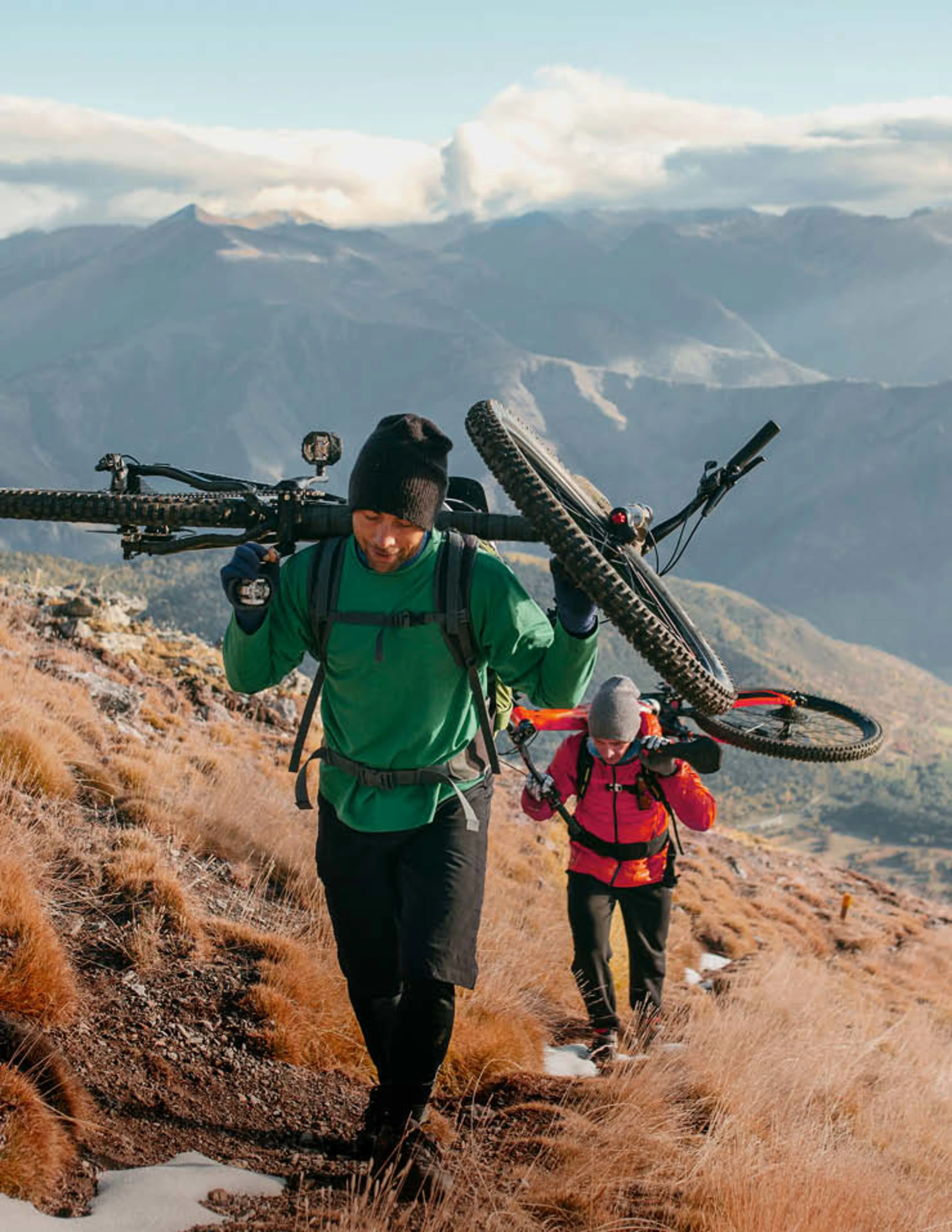 Ein Paar hat Mountainbikes auf die Schultern genommen, um diese einen Berg hinauf zu tragen.