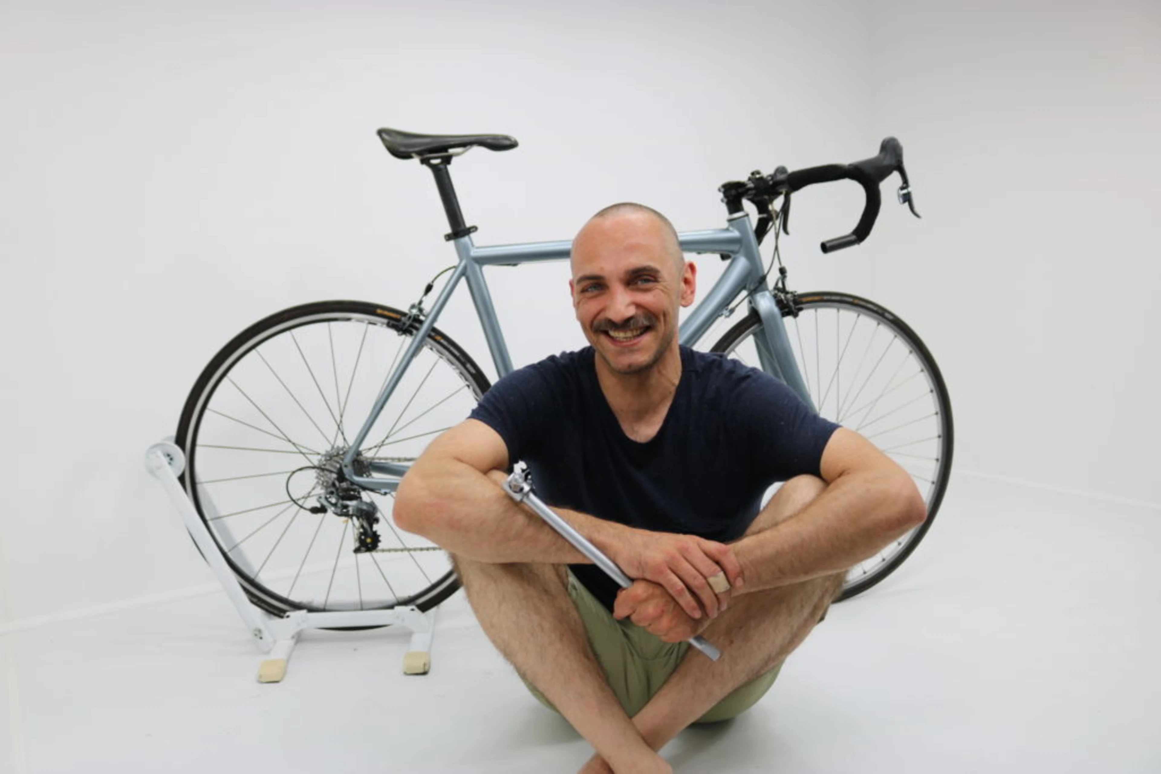 Mann mit Werkzeug in seiner Hand sitzt vor einem Fahrrad.