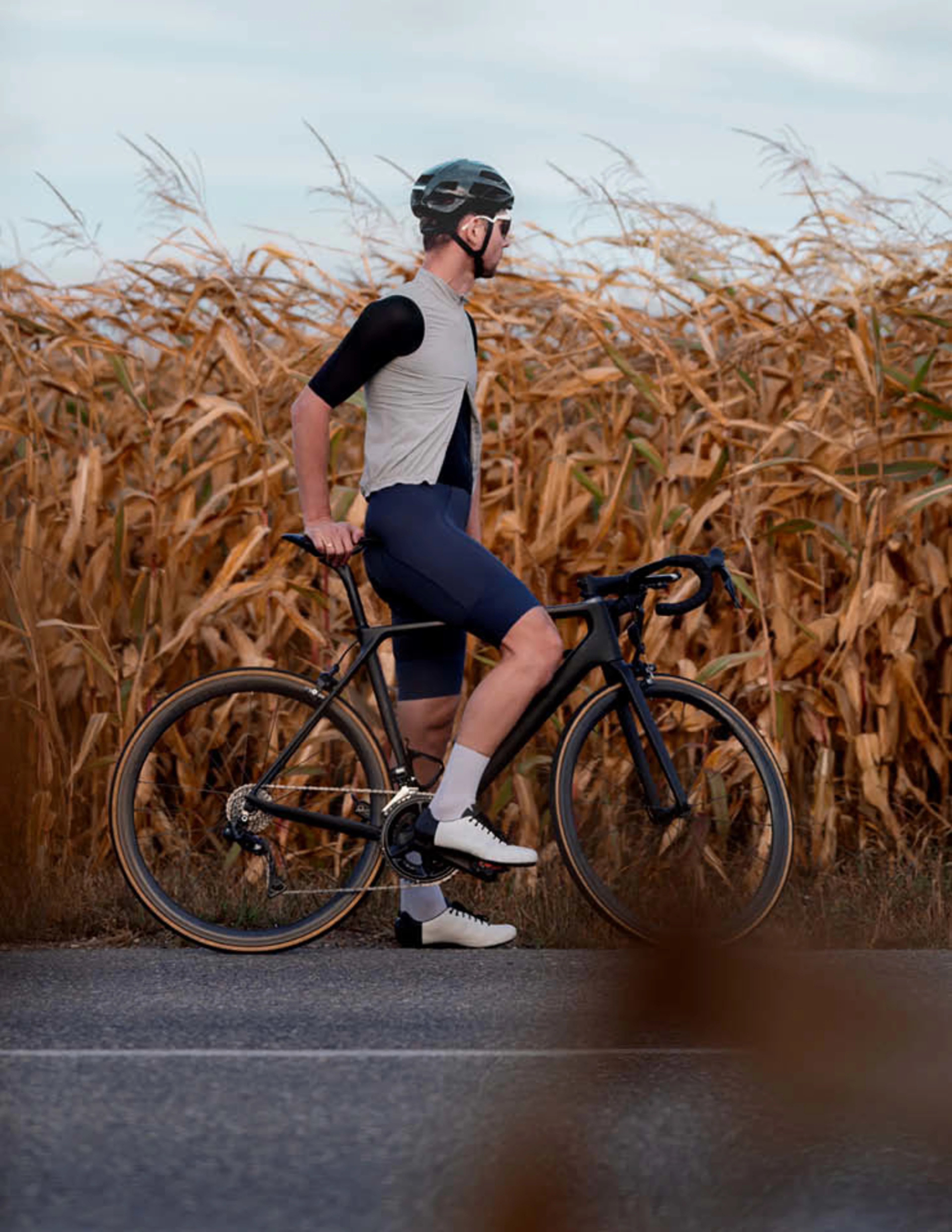 Ein Rennradfahrer steht auf der Straße von einem Kornfeld.