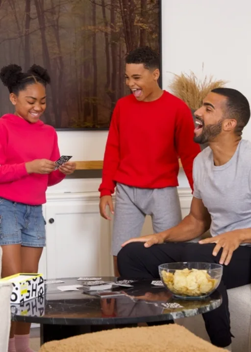 It's family game night! Dad and the two kiddos are gathered around the living room couch and coffee table playing cards. There’s snacks and fun to be had by all. Dad is wearing a grey t-shirt. Little brother and sister must be cold because they are both wearing fleece sweatshirts. Everyone is happy though because they are wearing Fruit of the Loom and spending time together as a family!