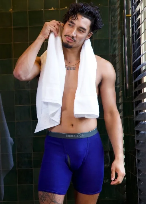 A man getting out of a fancy emerald color tile shower. He is shirtless with a white towel draped around his shoulders. He is wearing royal blue color CoolZone boxer briefs that have a grey waistband to them with Fruit of the Loom written on them.  He has his arm bent wiping at his hair because he just got out of the shower.. In his underwear as one does.