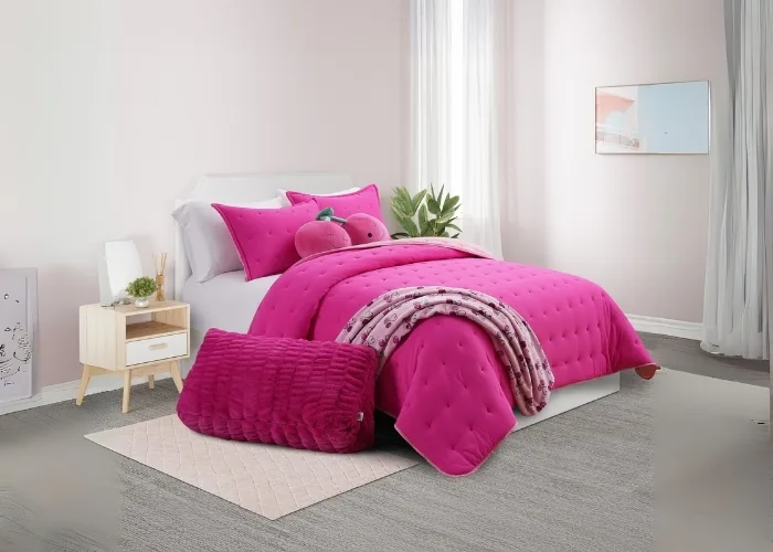 Bed room scene. There is a bed in the center. with a night stand on one side and a tall green plant next to it. There are curtains on the wall with a picture between the curtains. The bed is white. It is sitting on a light pink rug. The bedding is bright pink with matching bright pink pillows and a throw pillow that is in the shape of two cherrys, yes the fruit, this is fruit of the loom after all! On the  floor there is a wedge pillow that is pink, it is large and something you would use to lean up against.