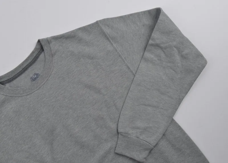 Pretty simple photo. Grey background with a darker grey crew neck sweatshirt laying down. One arm of the sweatshirt is folded in where its resting on the body of the sweatshirt. Only like 3 quarters of the sweatshirt is in frame of the photo. 