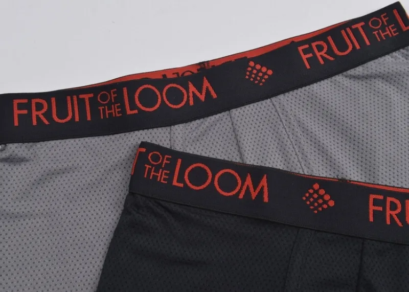 Grey background with two pairs of men's boxer briefs where you only see about from the fly up of the underwear. The first pair is a grey mesh with a black waistband that has red writing that reads Fruit of the Loom. The second pair laying on top you see even less of, just enough to see that they are made of a black mesh and then only like 3 inches of the waistband which is the same as the grey pair they are laying on.