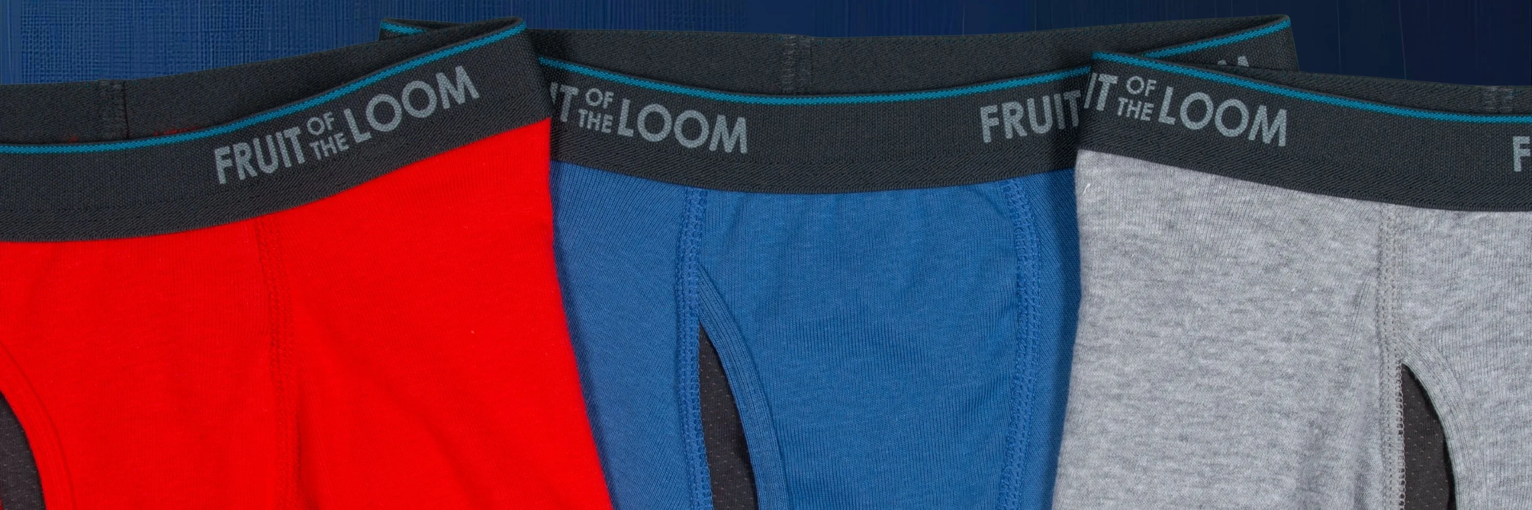 Three pairs of mens boxer briefs that are zoomed in where you see the waistband and then down to just the fly area of the boxer briefs. The waistbands are black all say Fruit of the Loom on them in grey. The very top of the waistband has a blue stripe. Each pair of boxers is a different color. The first pair is red, then blue, then grey.