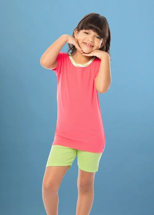 Young girl standing in front of an ombre blue studio backdrop. She is wearing coral and green pajamas. The top is coral with a lime green neck. The bottoms are solid lime green shorts.