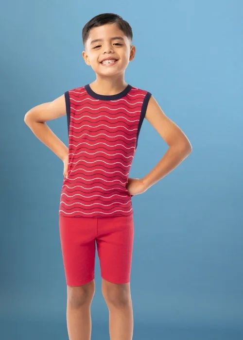 Young boy standing in front of an ombre blue studio backdrop. He is wearing red pajamas. The shirt is a tank style with wavy lines. The bottoms are solid red shorts. 