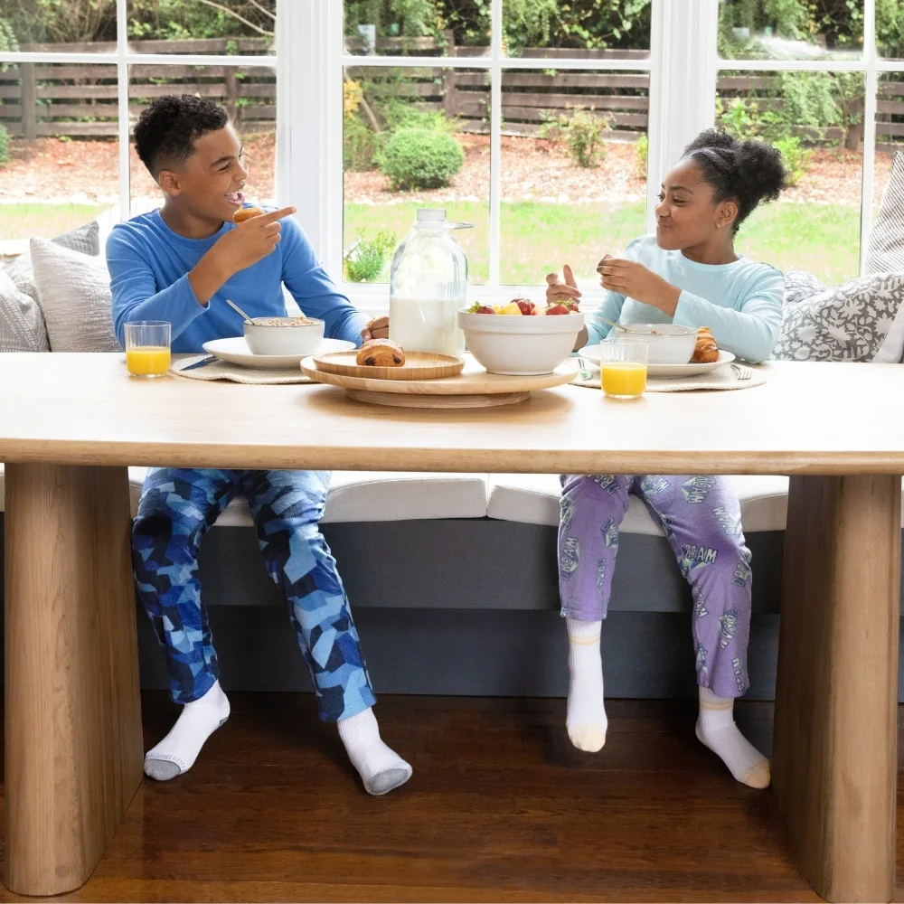 Young brother and sister sitting at a table eating breakfast. There is a window behind them showing that is a bright, sunny, happy day outside. The brother and sister are both wearing Fruit of the Loom kids pajamas. They are comfy and happy and enjoying breakfast. Best of all, they are getting along!
