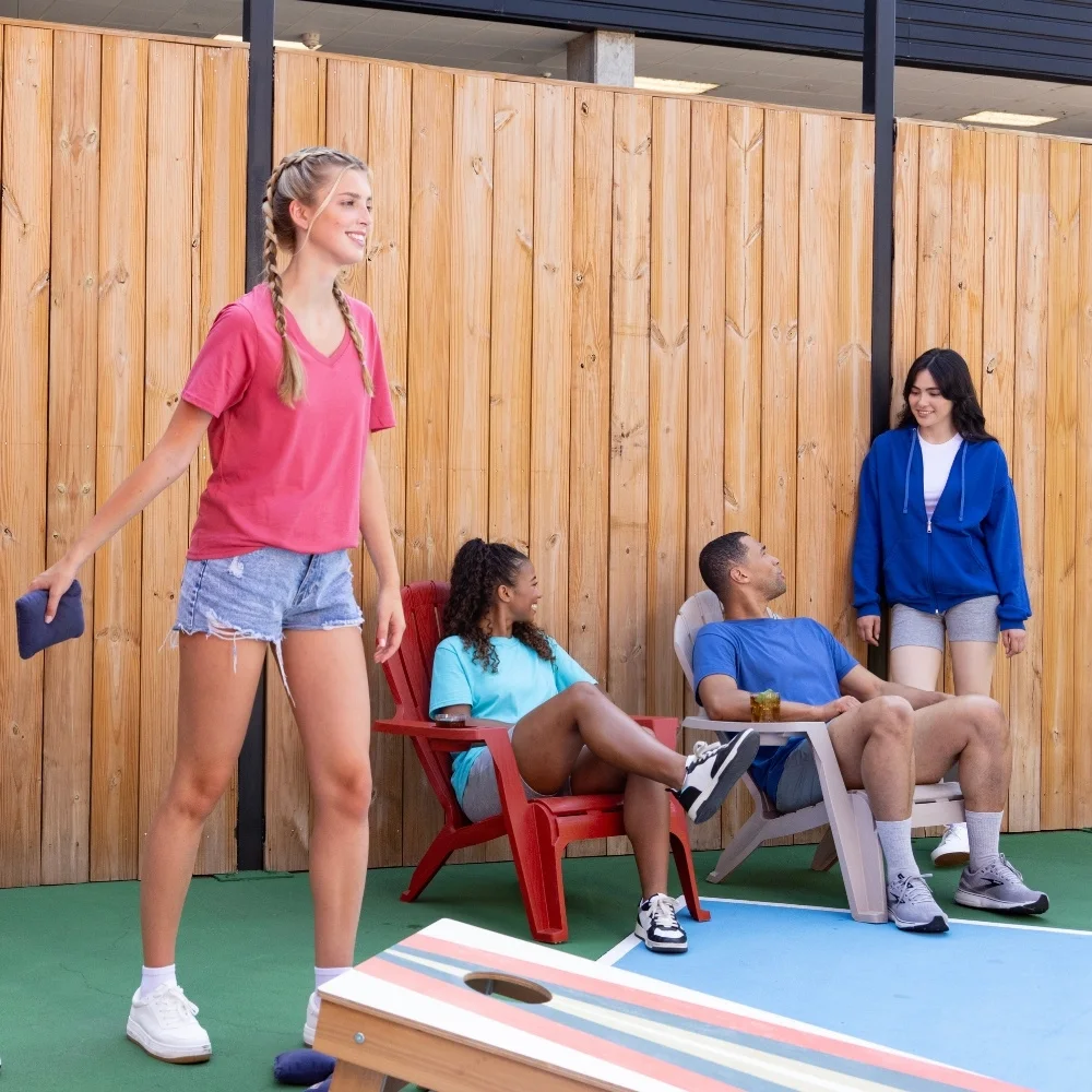 three women wearing fruit of the loom tees and sweatshirts playing cornhole