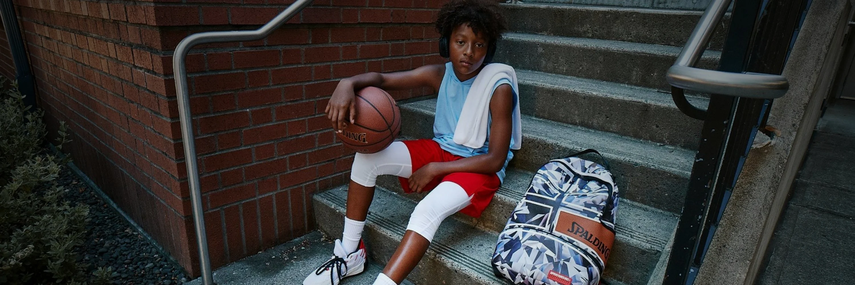 boy sitting on concrete steps holding a spalding basketball