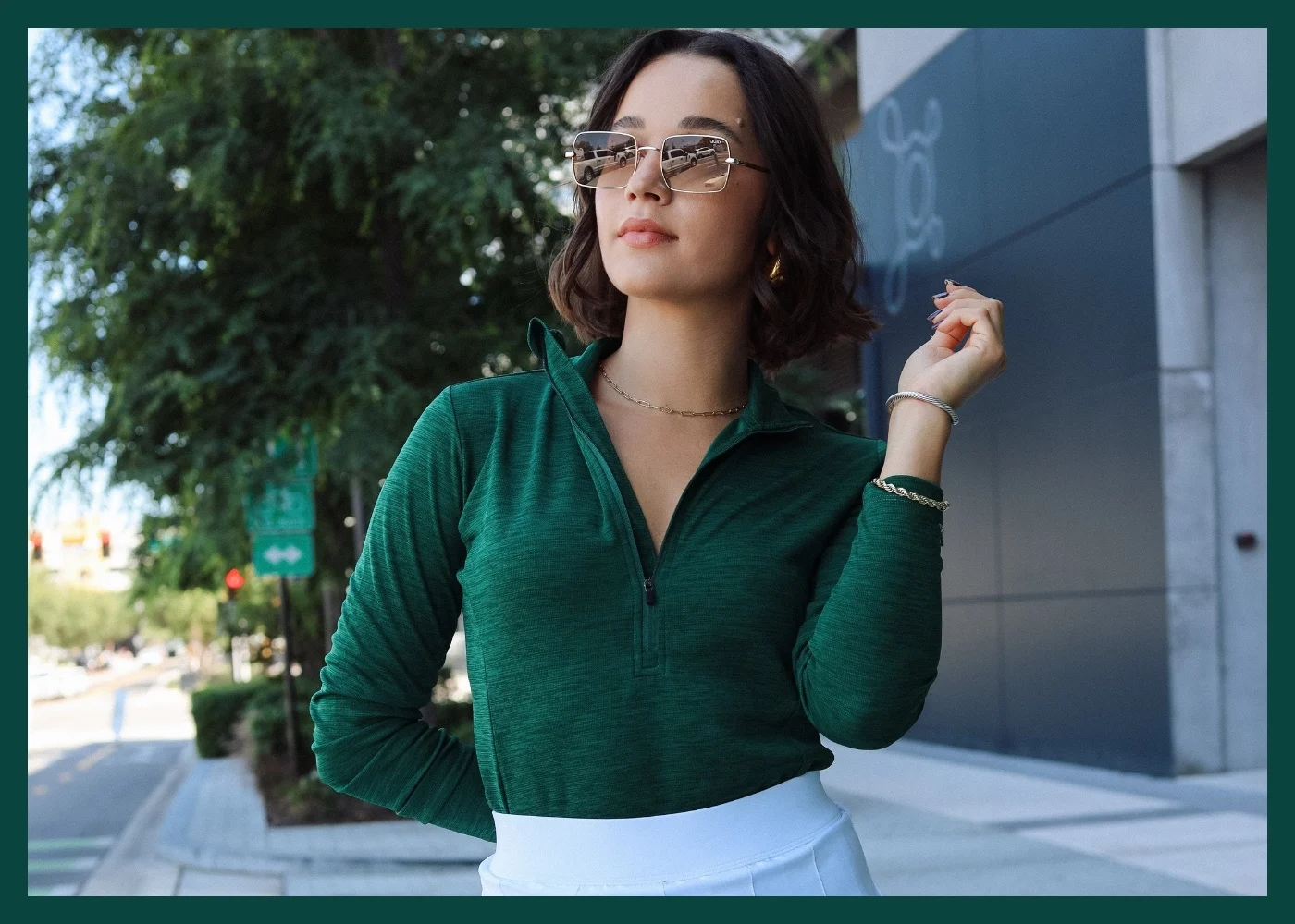 Female model wearing green polo, white skirt, and sunglasses