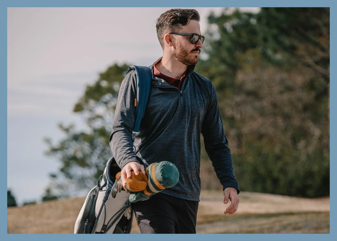 Male model wearin grey polo and grey pants, holding a putter on a green.