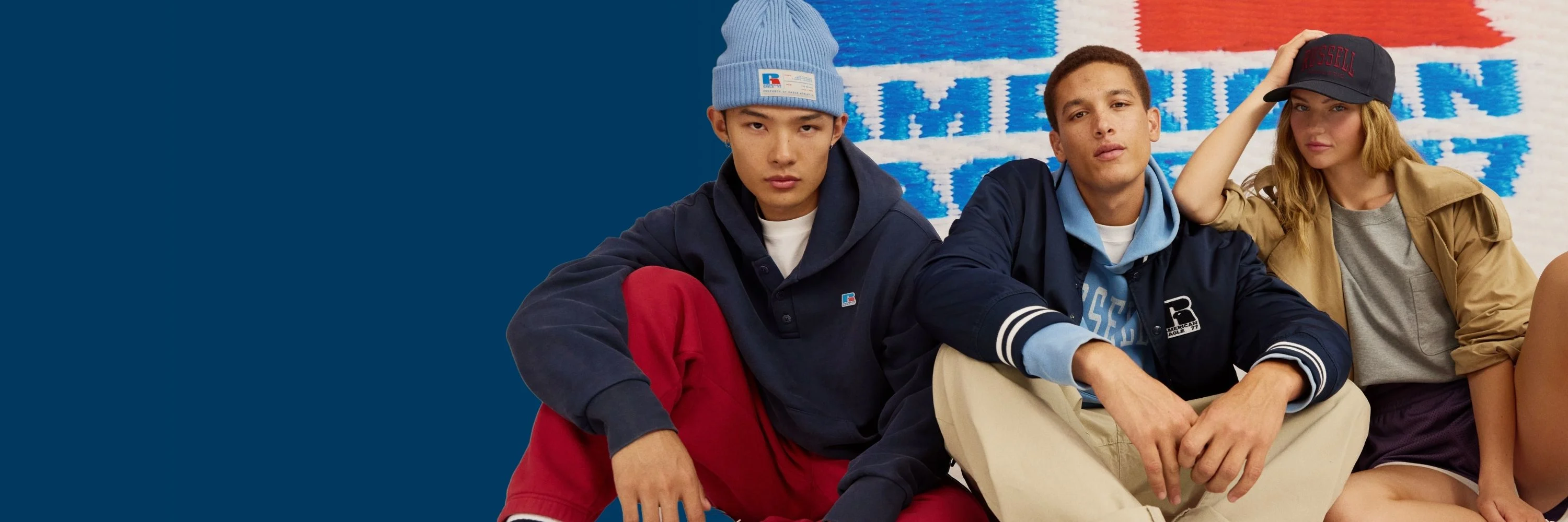 Two people wearing red sweatshirts standing against a red striped holiday background with a silver bow.