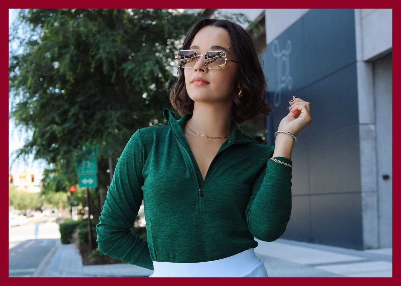 Female model wearing green polo, white skirt, and sunglasses