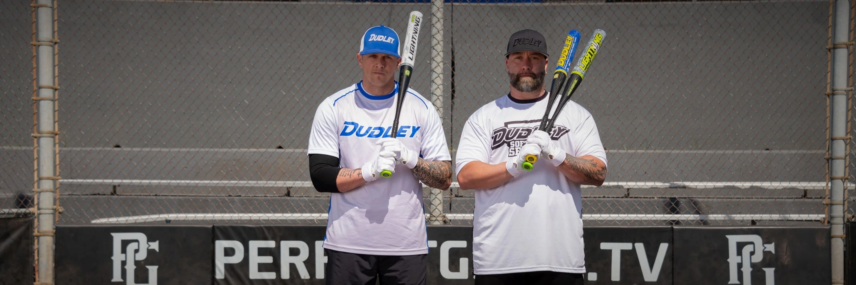 two male softball players standing in a softball field holding Dudley slowpitch bats