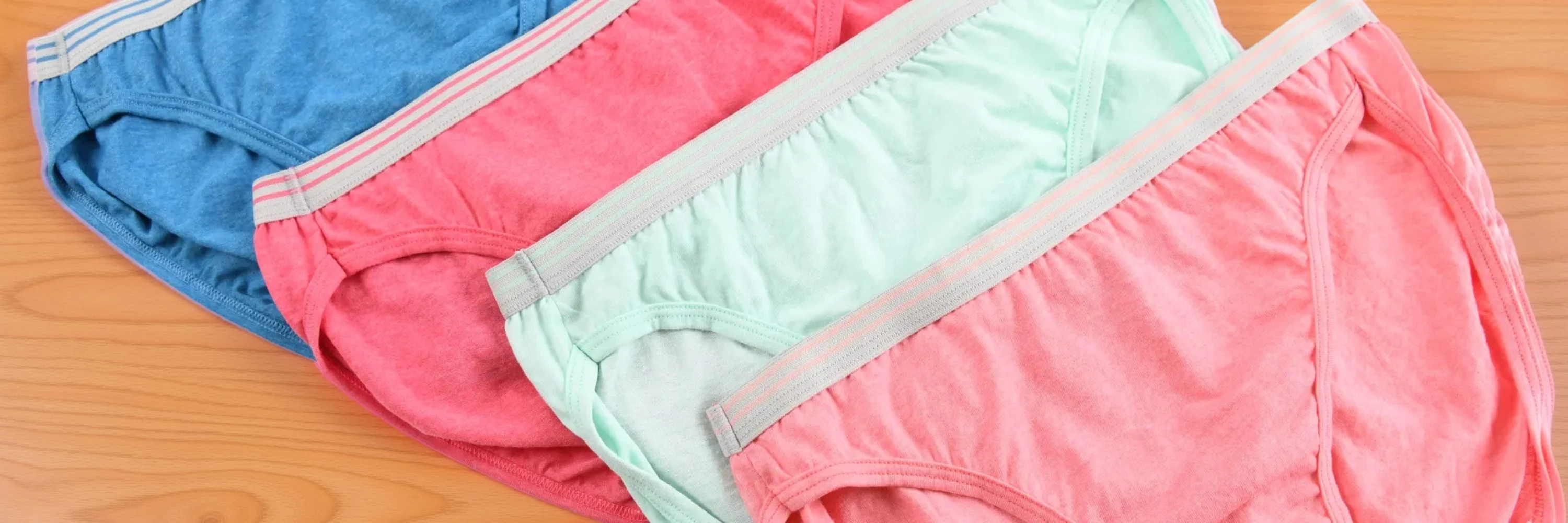 Assorted women’s cotton bikini underwear with elastic waistbands in blue, red, mint, and pink, laid out on a wooden background to highlight fit, fabric, and color options.