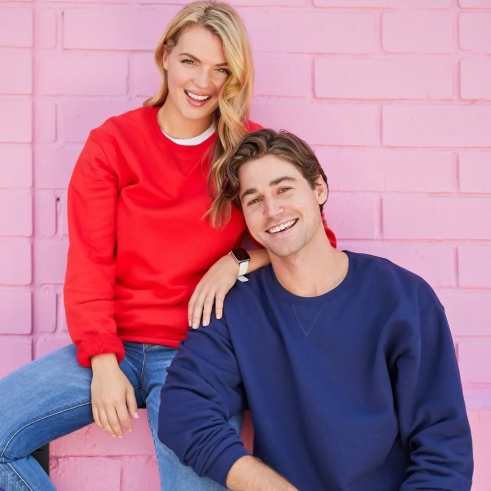 Two people in  red and blue sweatshirts and jeans, standing against a pink wall, showcasing casual Valentine’s couple loungewear.