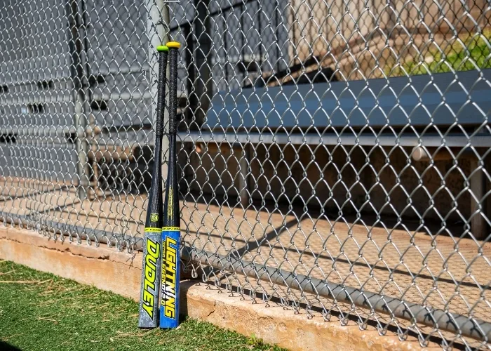 Dudley softball bats leaning on a fence outside a softball field.