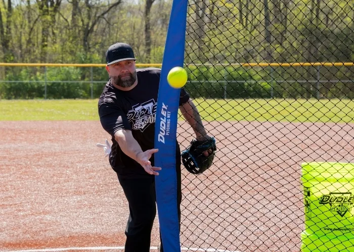 softball player tossing a softball into a pitching net.