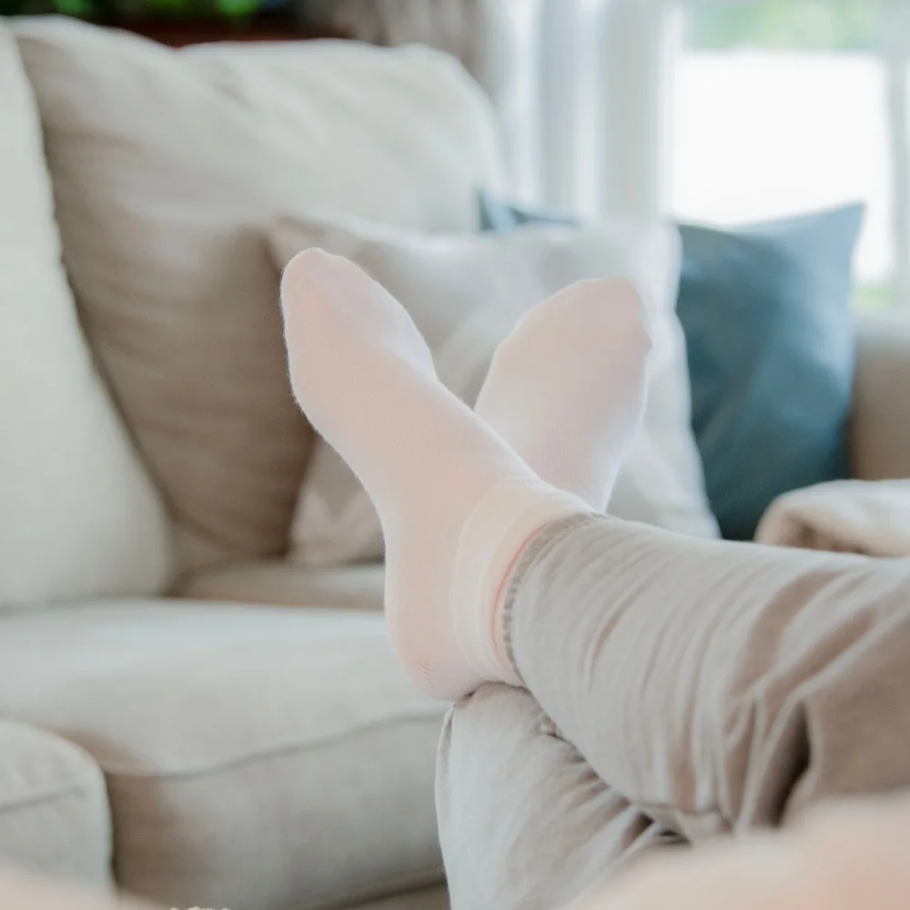 Feet resting on a sofa while wearing white Fruit of the Loom socks in a comfortable home setting.  Alternate option: