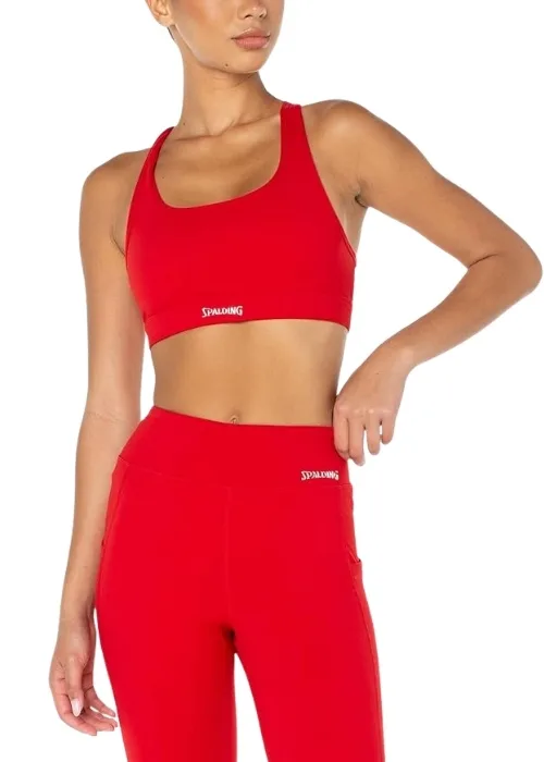 Model wearing a red Spalding sports bra and matching high-waisted leggings standing in a modern gym with mirrors and a dumbbell rack in the background.