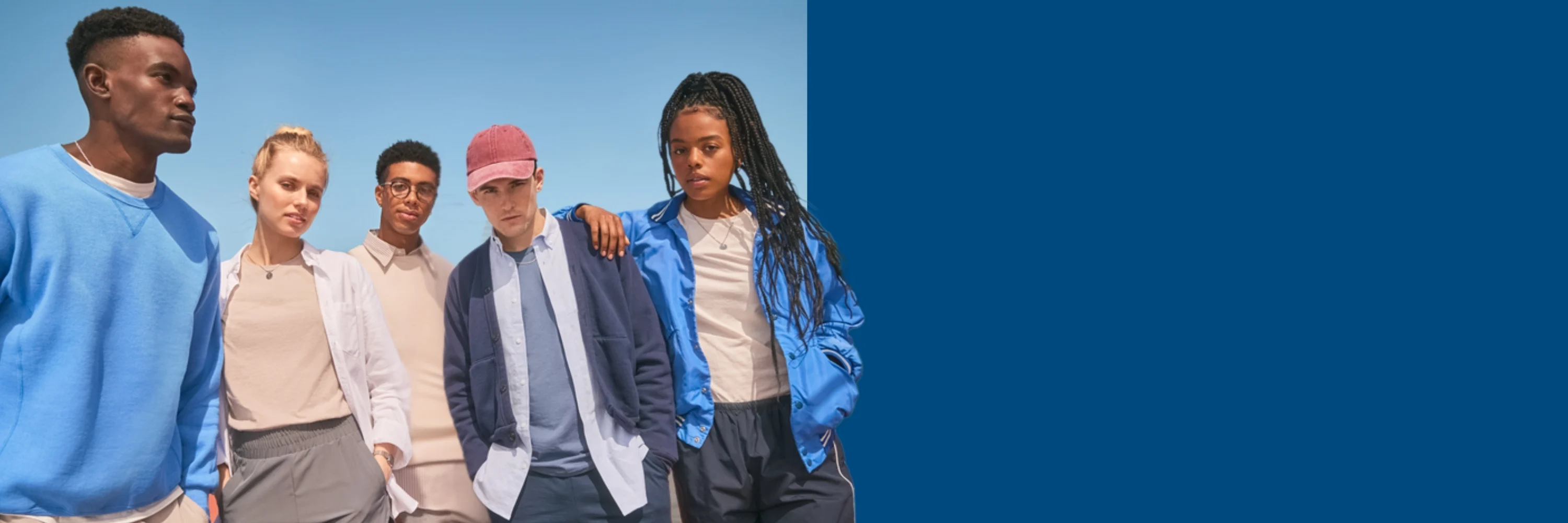 Four people wearing Russell Athletic athletic-inspired apparel, including shorts, track pants, lightweight layers, and a blue jacket, standing together on an outdoor track under a clear blue sky.