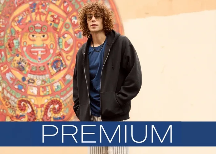 Person wearing a black zip-up hoodie layered over a blue T-shirt, standing outdoors in front of a colorful mural. With Text Overlay that says premium